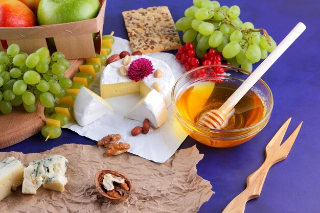 Food for a healthy and tasty snack on a purple background Camembert with berries fruits honey and nuts on a wooden board Closeup