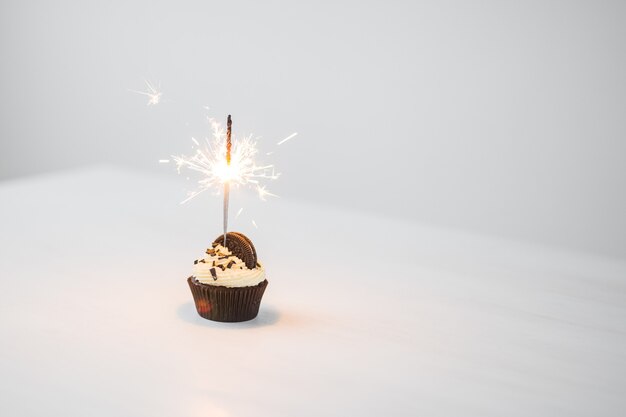 Food and holiday concept - Birthday cupcake with sparkler over white background with copy space.