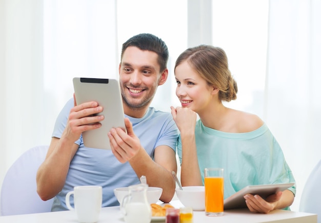 food, home, couple and technology concept - smiling couple with tablet pc reading news and having breakfast at home