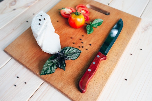 Food ingredients. Basil cheese tomatoes and knife on wooden board