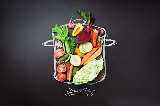 Food ingredients for blending creamy soup on painted stewpan over black chalkboard. 