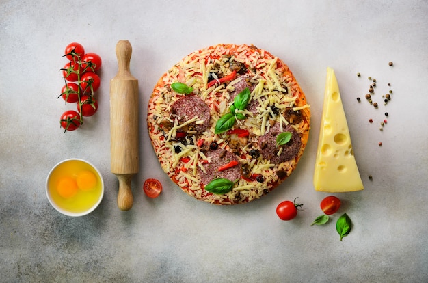 Food ingredients for italian pizza, cherry tomatoes, flour, cheese, basil, rolling pin, spices on light grey. 