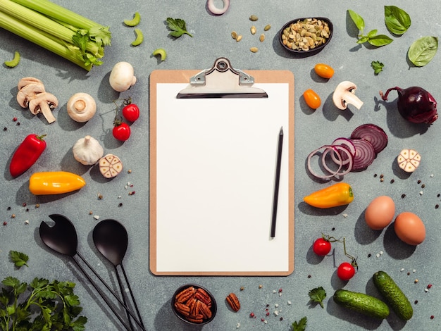 Food ingredients salad serving utensils and clipboard with white paper sheet Various of vegetarian cooking ingredients on gray background Diet menu concept Copy space for text Top view flat lay