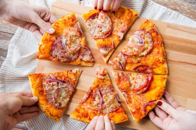 food, italian kitchen and eating concept - close up of hands taking and sharing homemade pizza on wooden table