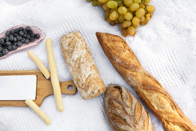 Food lay out on picnic blanket. fresh baked bread, grapes and photocam lay on white blanket