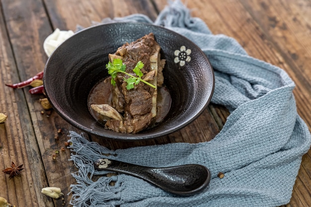 The food made of beef is in the bowl on the cloth of the wooden table