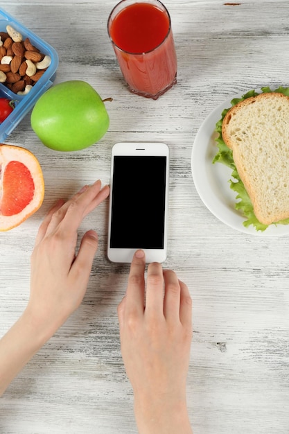 Еда и мобильный телефон в женских руках на деревянном фоне