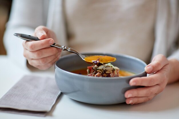 еда, новая скандинавская кухня и концепция людей - женщина ест овощный тыквенно-имбирный кремовый суп с козьим сыром и томатным салатом с йогуртом в миске в кафе или ресторане