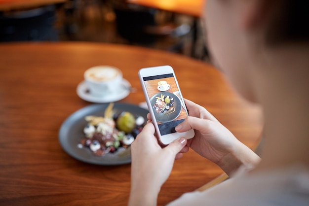 food, new nordic cuisine, technology and people concept - woman with smartphone photographing chocolate ice cream dessert with blueberry kissel, honey baked fig and greek yoghurt at cafe