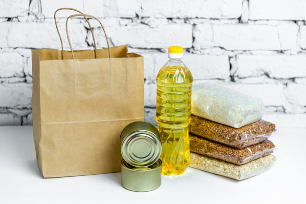 Food in a paper bag for donations, on a white brick background.\
anti-crisis stock of essential goods for the period of quarantine\
isolation. food delivery, coronavirus.