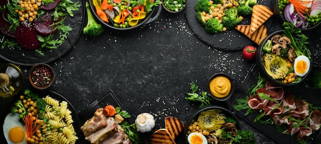 Food pasta pork ribs avocado Buddha bowl and beet salad on a black stone background Top view Free space for text