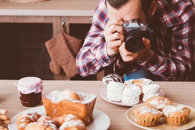 フードフォトグラフィー。自家製の甘いパン屋。焼きたてのペストリーの写真を撮るカメラを持つ男。