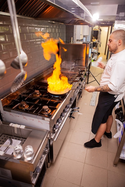 Food preparation. Chef cook in kitchen with pan over stove doing flambe.Crazy chef cooking with big fire on the frying pan.