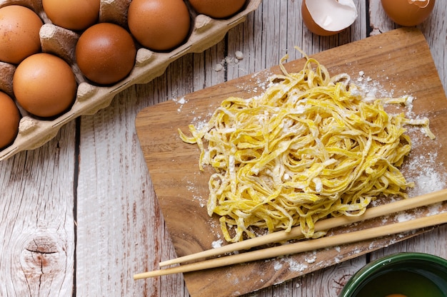 Preparazione del cibo - tagliatelle all'uovo crude con farina in polvere sul tagliere di legno arrotondato con le uova