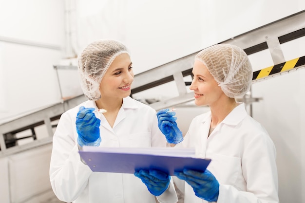 食品生産産業人々コンセプト - クリップボードで幸せな女性技術者工場でアイスクリームの品質を味わう