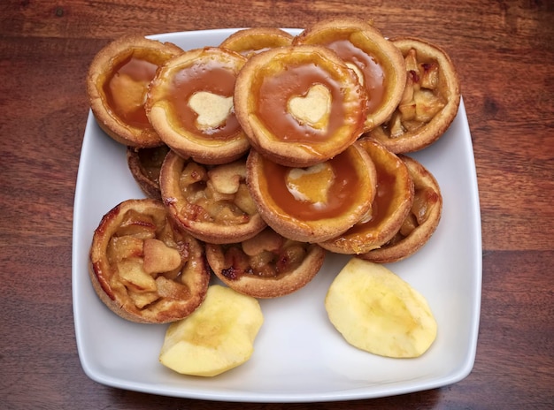 FOOD, small jam tarts with apples in a white plate on a wooden table