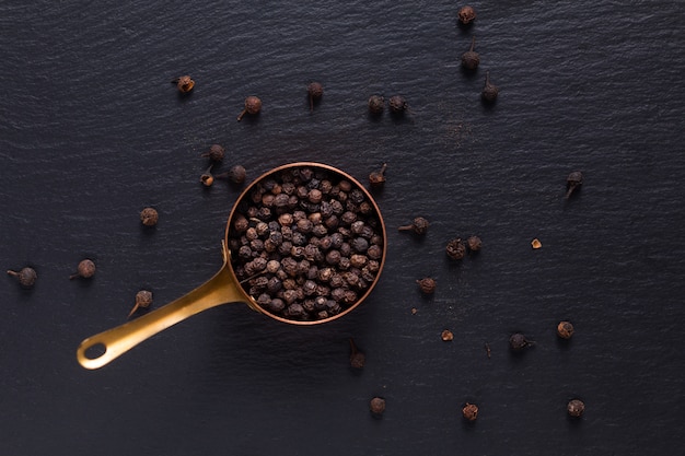 Vista superiore di concetto di spezie alimentari di pepe nero organico in tazza di rame su pietra ardesia nera con spazio di copia