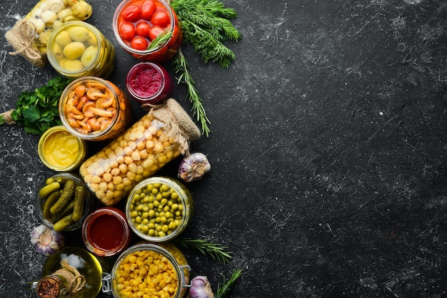 Food stocks in glass jars Pickled vegetables On a black background Top view