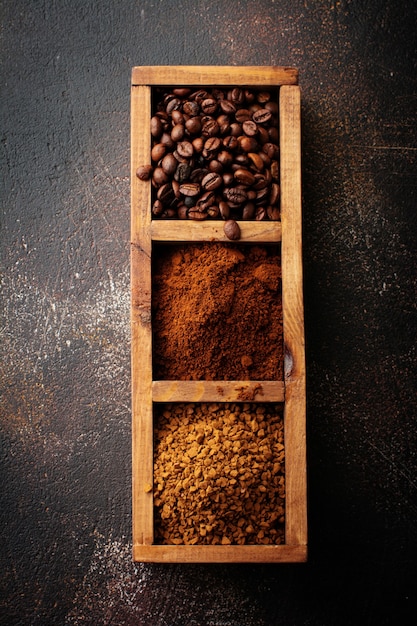 Food surface with three kinds of coffee: beans, milled, instant in wooden box on old concrete brown surface. Rustic stile. Selective focus. Top view.