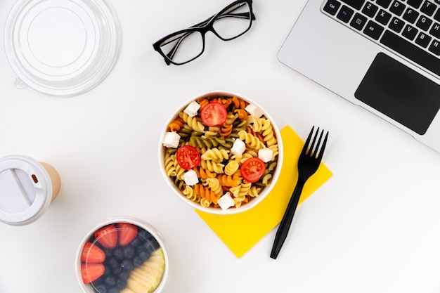 Food in taking away boxes on white table with laptop.