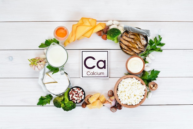 Photo food with calcium. a variety of foods rich in calcium: cheese, milk, parmesan, sour cream, fish, almonds, parsley, garlic, broccoli. on a white wooden background. top view. free copy space.