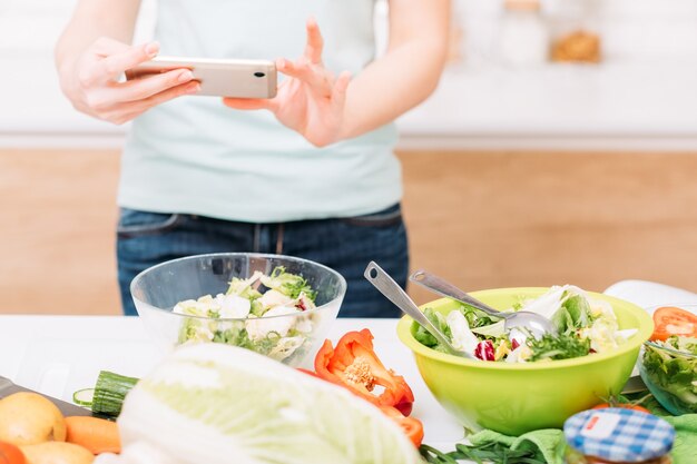 Foodblogger. Gezonde voeding. Salade schalen met verse groenten. Vrouw met smartphone bijgesneden schot.