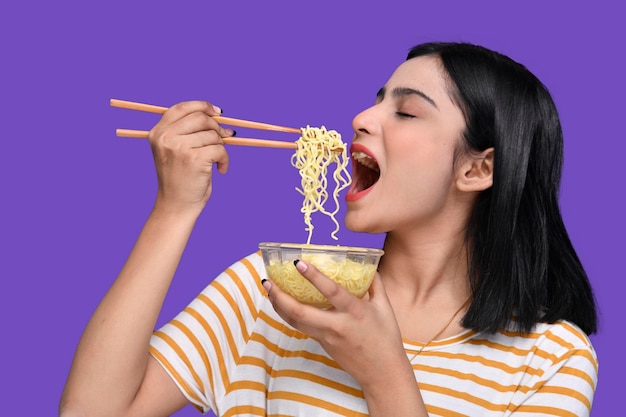 紫色の背景の上の麺を食べる食通の女の子インドのパキスタンのモデル