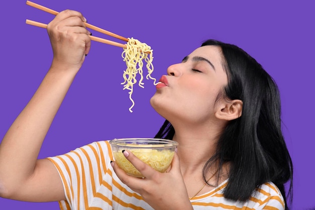 紫色の背景の上の麺を食べる食通の女の子インドのパキスタンのモデル