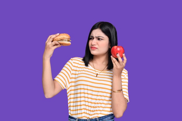 Foodie girl holding apple and burger looking at junk food indian pakistani model