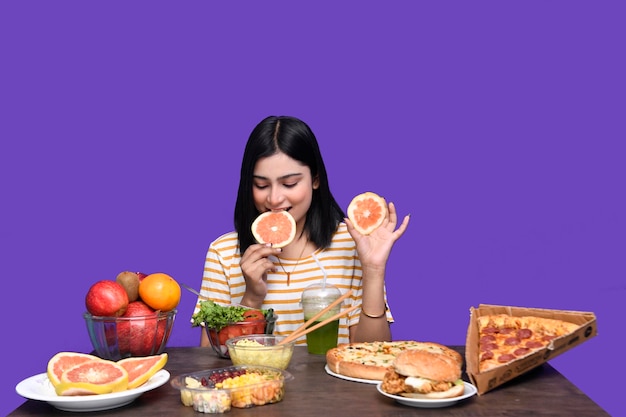 Фото Гурман девушка сидит за фруктовым столом улыбается и ест цитрусовые индийская пакистанская модель