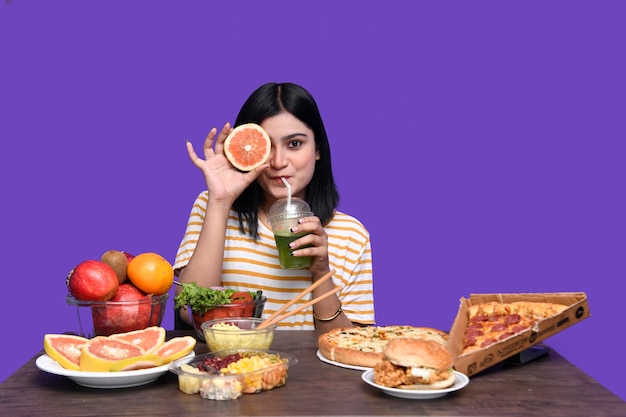 Фото Гурман девушка сидит за фруктовым столом улыбается, держа цитрусовые фрукты индийская пакистанская модель