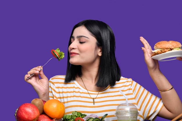 foodie girl sitting at fruit table eating salad and hand stop sign to burger indian pakistani model