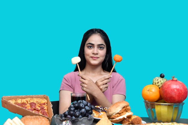 Photo foodie girl sitting at fruit table smiling and holding sweet candy indian pakistani model