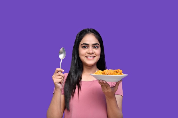 紫色の背景のインドのパキスタンのモデルの上にスプーンとビリヤニを持って笑っている食通の女の子