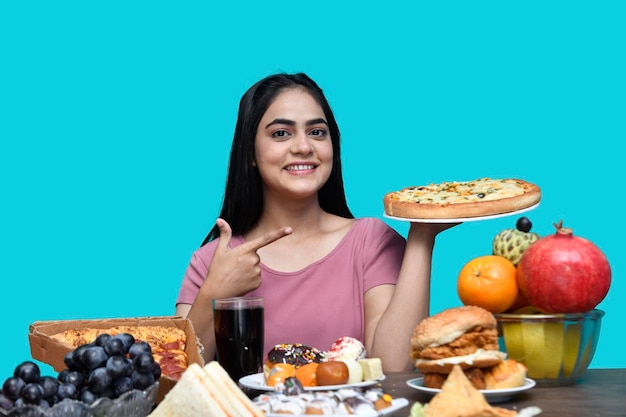 foodie meisje zit aan de fruittafel glimlachend en houdt een pizza indiaans pakistaans model vast