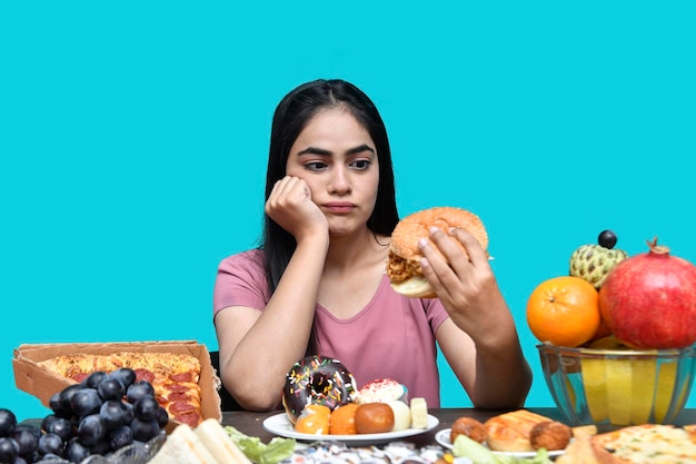 foodie meisje zit aan fruittafel met hamburger schokkend Indiaas Pakistaans model