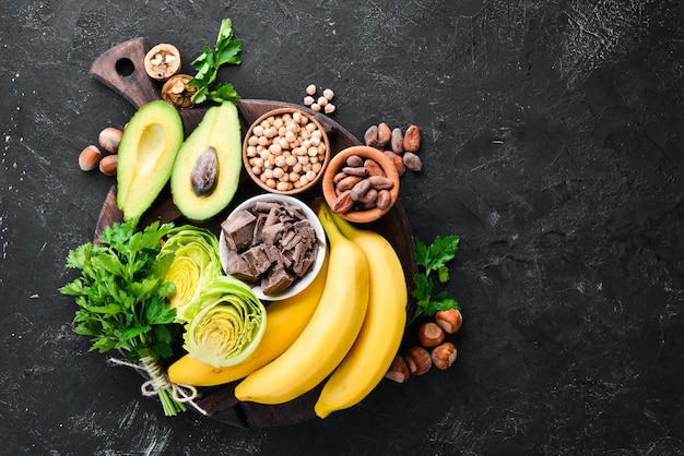 Foods containing natural magnesium. Mg: Chocolate, banana, cocoa, nuts, avocados, broccoli, almonds. Top view. On a black background.