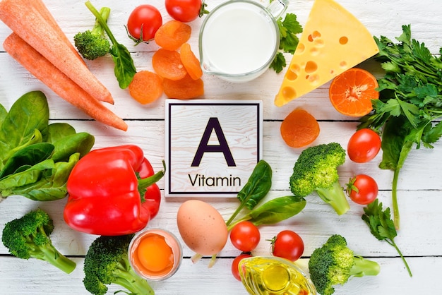 Foods containing natural Vitamin A broccoli carrots milk cheese spinach apricots parsley tomatoes On a white wooden background Top view