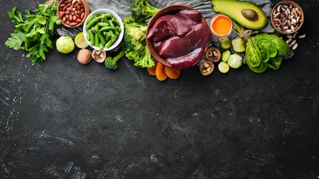 Foods that contain natural vitamin B9 Liver avocado broccoli spinach parsley beans nuts on a black stone background Top view