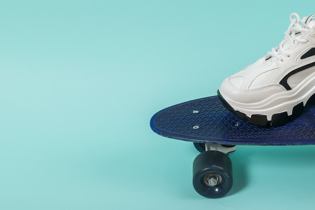 Foot in a white sneaker on a blue skateboard. Sports style.