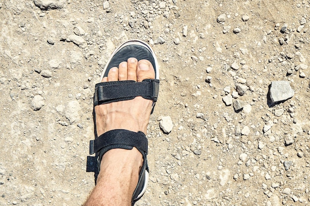 Photo foot of young man in sports black sandal stands on sea beach covered with light grey rocks