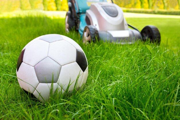 A football ball and a lawn mower in the green grass a closeup