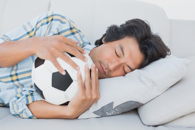 Football fan hugging ball on couch