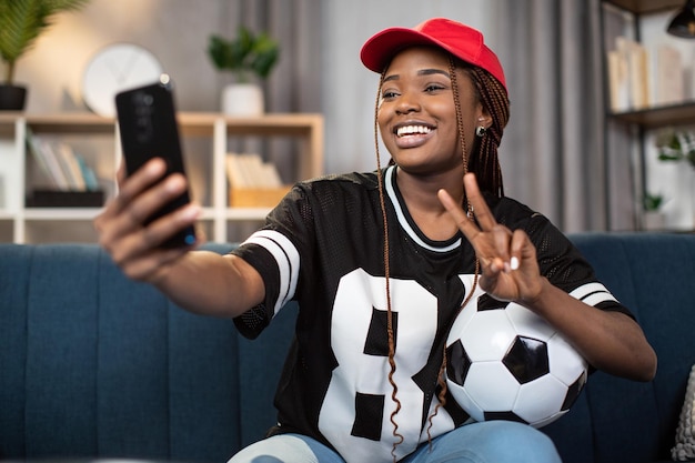 Football fan sitting on sofa and and taking selfie on mobile