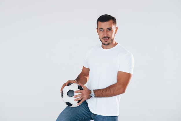 Football fan with soccer ball Young handsome man standing indoors against white background