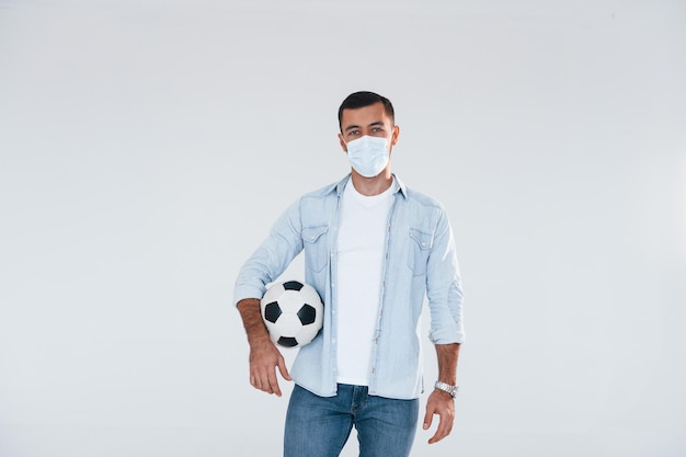 Football fan with soccer ball Young handsome man standing indoors against white background