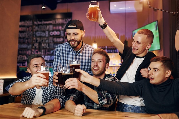 Football fans watching TV Group of people together indoors in the pub have fun at weekend time