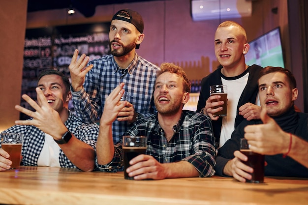 Football fans watching TV Group of people together indoors in the pub have fun at weekend time