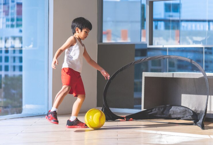 フットボール選手の少年は部屋でボールを踏んでいます。
