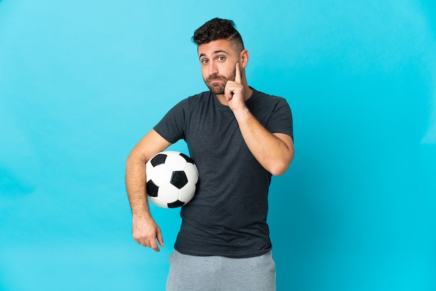 Football player isolated on blue wall thinking an idea